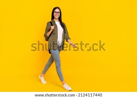 Full length photo of cute young lady go wear bag spectacles shirt jeans sneakers isolated on yellow background
