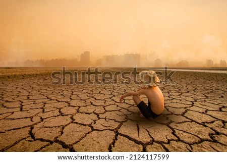 Young man sitting on drying river and looking to polluted city with smoke of co2, carbon dioxide on background. Metaphoric of Environment damage, Climate change and pollution. Royalty-Free Stock Photo #2124117599