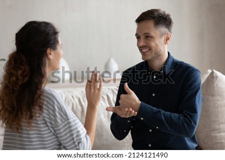 Smiling man and woman with deafness using signs for communication, sitting on couch at home, smiling. Therapist teaching gesture language to patient with disability. Hearing disorder concept Royalty-Free Stock Photo #2124121490