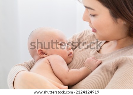 Selective focus Beautiful Asian mother holding newborn baby sleep on her lap, Young mom supports and tenderly cuddles adorable infant gently while infant sleeping on chest with safe and care.