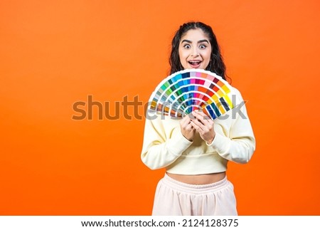 Beautiful surprised woman with color palette fun. Paint and painting concept. Interior designer woman holding color palette guide on orange background with copy space.