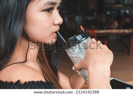 Candid shot of a beautiful young Filipina in an off-shoulder top sipping on her milk tea. At an al fresco cafe.