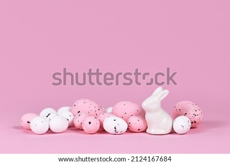 White and pink Easter eggs with small bunny sculpture on pink background with copy space