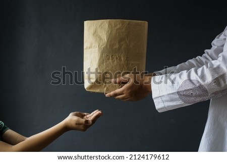 Ramadan kareem background concept. Muslim hand giving alms bag of rice isolated on gray background. Zakah fitrah Royalty-Free Stock Photo #2124179612