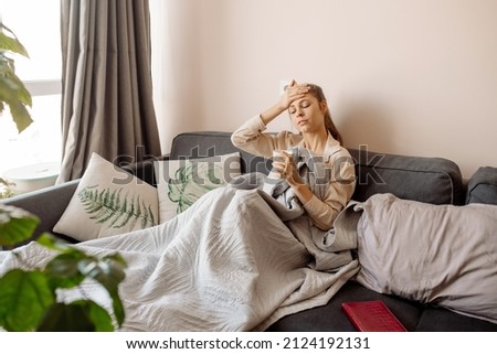 Young woman with long covid syndrome symptoms sitting at couch at home biophilic interior, many indoor trees	 Royalty-Free Stock Photo #2124192131