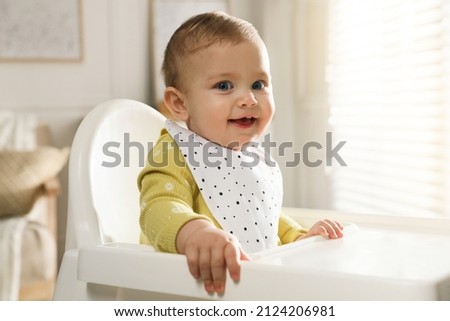 Cute little baby wearing bib in highchair at home Royalty-Free Stock Photo #2124206981