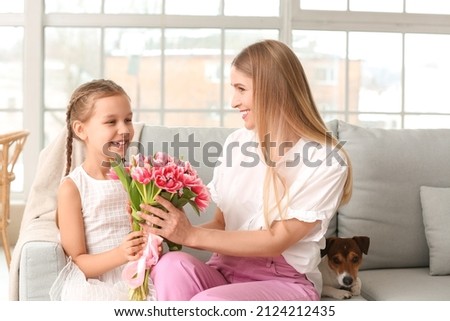 Little girl greeting her mother with tulips at home on holiday