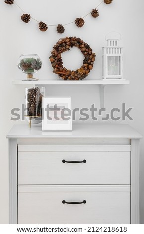 Pine cones, natural wreath and candles on chest of drawers in room