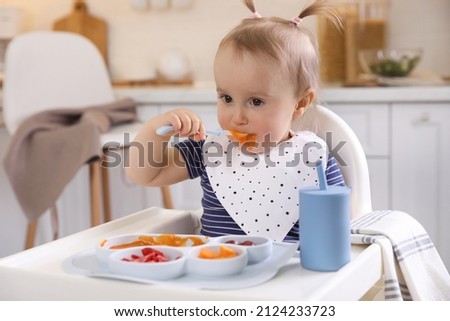 Cute little baby eating food in high chair at kitchen Royalty-Free Stock Photo #2124233723