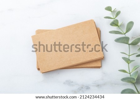 Stack of business cards kraft paper mockup on marble table with green leaf, top view