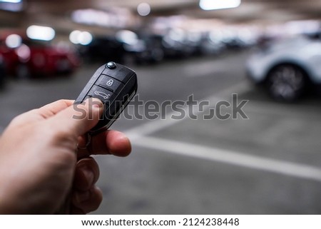Person holding car remote control in focus, busy full car park out of focus in the background. City life. Parking cost and automobile density issue. Royalty-Free Stock Photo #2124238448