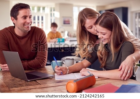 Parents Helping Teenage Daughter With Homework Sitting At Kitchen Table At Home Using Laptop Royalty-Free Stock Photo #2124242165