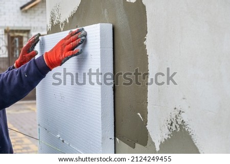 Construction worker installing styrofoam insulation sheets on house facade wall for thermal protection. Royalty-Free Stock Photo #2124249455