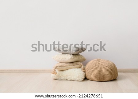 Beige pouf and cushions near light wall Royalty-Free Stock Photo #2124278651