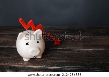 Sad piggy bank and down arrow. Savings and reserves decrease. Inflation, depreciation of assets. Falling income, lower wages. Falling GDP. Economic recession, crisis. Capital flight, worsening economy Royalty-Free Stock Photo #2124286856