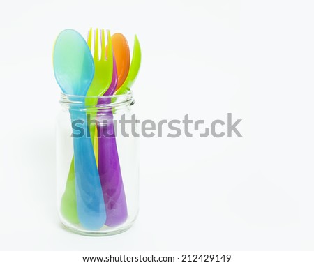 Colorful plastic spoons and forks in jar .