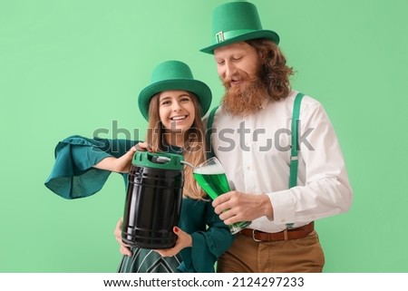Happy young couple with glass of beer and keg on green background. St. Patrick's Day celebration