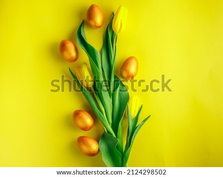 Easter golden eggs and tulips flat lay yellow background with copy space for text. Modern painted wooden easter eggs and spring flowers composition. Greeting card template, beautiful easter background