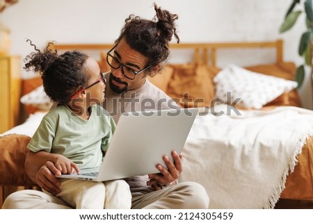Happy african american family little boy son with young dad watching funny videos on laptop together at home, father with child using computer in bedroom while enjoying weekend