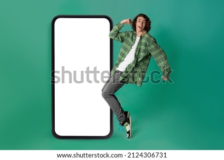 Happy guy dancing near big smartphone with blank white screen, recommending new mobile app, promoting online offer or website, green background, mockup