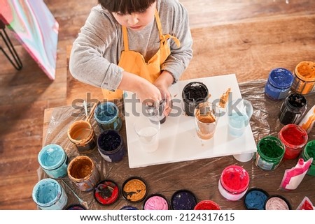 Serious little boy throws his hands into the paints while drawing pictures on the canvas
