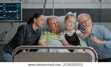 Family taking pictures with old patient in hospital ward, using mobile phone in visit. Niece and woman taking selfie on smartphone with sick pensioner and visitors. Little girl visiting grandma