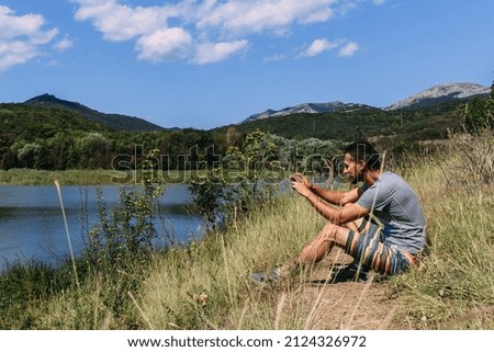 Man on the shore of the lake alone and takes a photo on his smartphone