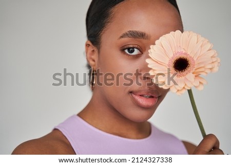 Brunette multiracial woman closed one eye with the flower while looking at the camera