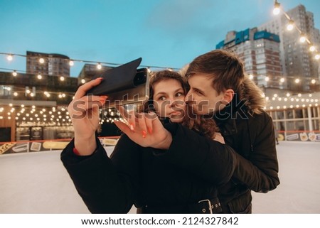 A young couple in love hugs and takes a selfie on an ice rink.