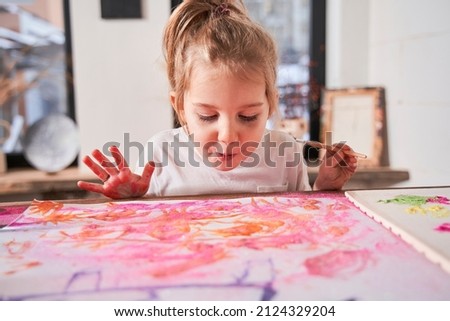 Caucasian child girl blowing at the picture with glitter while creating at the art school