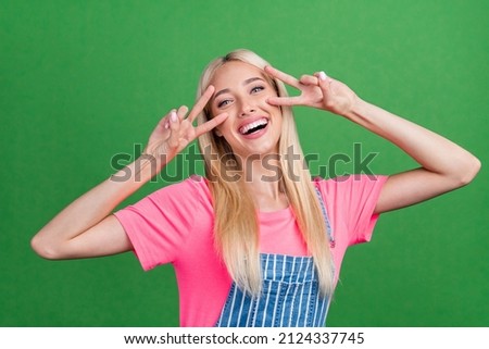 Photo of funny positive charming lady show v-sign symbol have fun wear striped overall isolated green color background