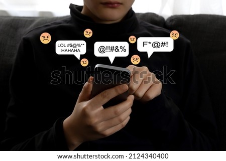 A teenager using smartphone alone reading bad comments, text negative emoticons pop up above the screen. Teen mental health problem, social media harassment concept.  Royalty-Free Stock Photo #2124340400