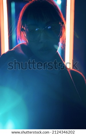 Dark silhouette of stranger woman standing in neon lights. Cyberpunk girl in spectacles at modern glow night city.
