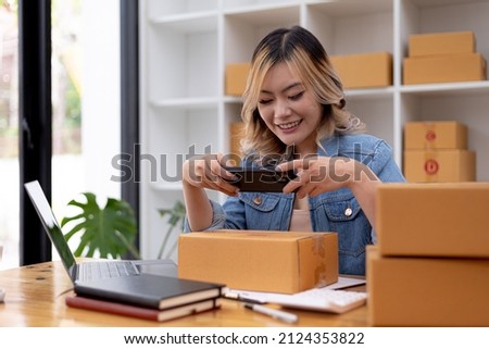 A woman using a smartphone to take pictures in front of parcel boxes, parcel boxes for packing goods, delivering goods through private courier companies. Online selling and online shopping concepts.