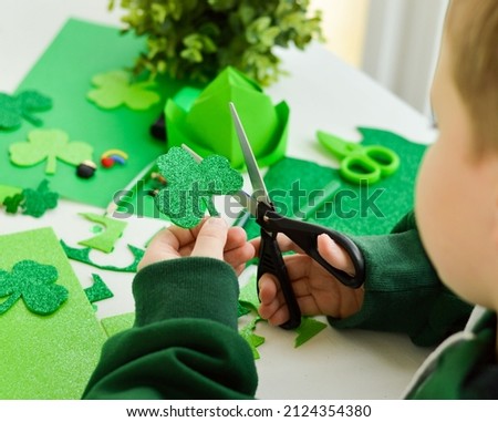 DIY St.Patricks Day decor. Happy boy make craft card from shamrocks of shiny green paper. Selective focus