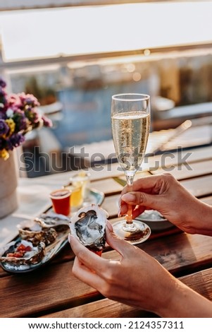 Woman eating fresh oysters and drinking chilled prosecco wine on the summer sunset. Seafood delicacies