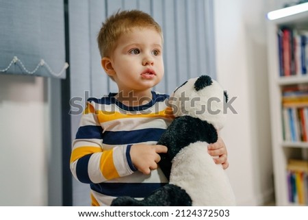 Waist up portrait of one small caucasian boy two years old holding panda toy while standing alone at home looking to the side copy space childhood and growing up concept Royalty-Free Stock Photo #2124372503