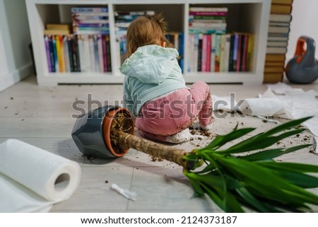 one caucasian baby girl making mess playing and mischief with bad behavior ripping paper towel and flower pot cruched on the floor naughty kid at home childhood and growing up misbehavior concept Royalty-Free Stock Photo #2124373187