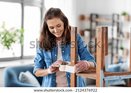 repair, diy and home improvement concept - happy smiling woman sticking adhesive tape to old wooden table or chair for repainting it Royalty-Free Stock Photo #2124376922