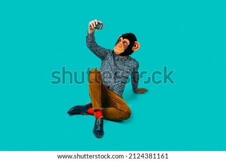 man, wearing a monkey mask and colorful clothes, taking a selfie with a retro film camera, sitting on a blue background with some blank space around him