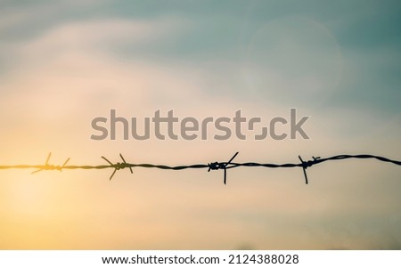 Barrier wire fence with sunset Twilight sky. Chain spike for world war safe security boundary concept for human rights slave, prison hostage hope to peace. International liberty day. russia ukraine Royalty-Free Stock Photo #2124388028