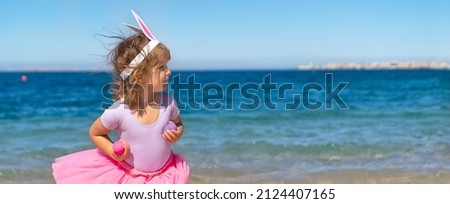 Cute girl holding colorful eggs in her hands, standing near the sea. Happy Easter holidays concept. Copy space