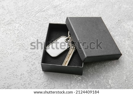 Key with stylish keychain in box on light background