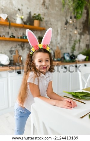 
A little cute girl with rabbit ears stands in the kitchen while preparing for the Easter celebration.