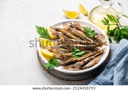 Pan-fried anchovies in the white plate with lemon and parsley. White background, blue runner. Copy space. Royalty-Free Stock Photo #2124418793