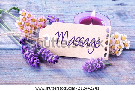 Spa massage background with fragrant fresh lavender and flowers with a burning aromatherapy candle around a label or gift tag with the script - Massage - on rustic blue boards