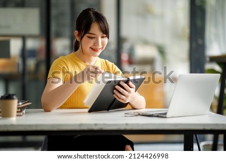 Shot of young asian female Asian young woman student sitting at table and writing on notebook. Young female student studying or reading in Coffee shop.