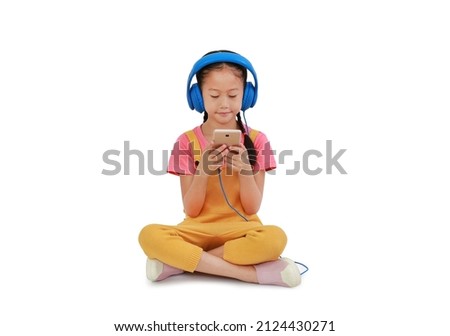 Asian little girl child wearing headphones and enjoy with smartphone sitting isolated on white background. Image with Clipping path