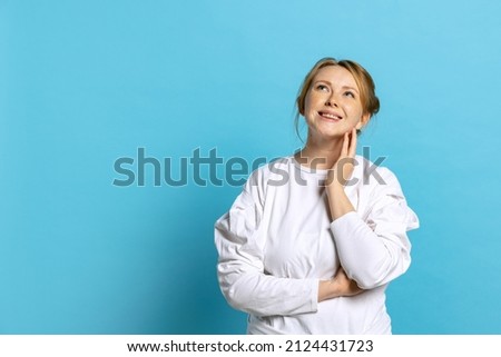 Dreaming young beautiful girl wearing white pullover looking up isolated on blue background. Concept of emotions, facial expression, youth, inspiration, sales. Copy space for ad