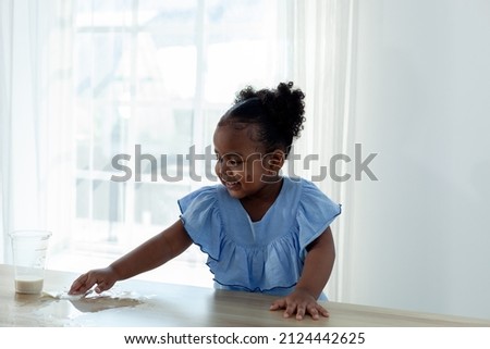 cute little girl spilling milk on the table and happily clean the table.